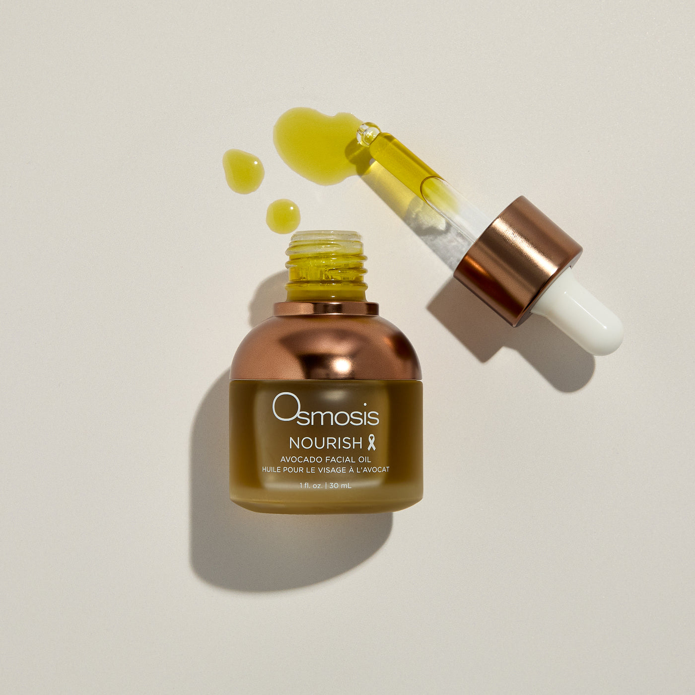 Osmosis Nourish avocado facial oil with dropper and product drops on a beige background