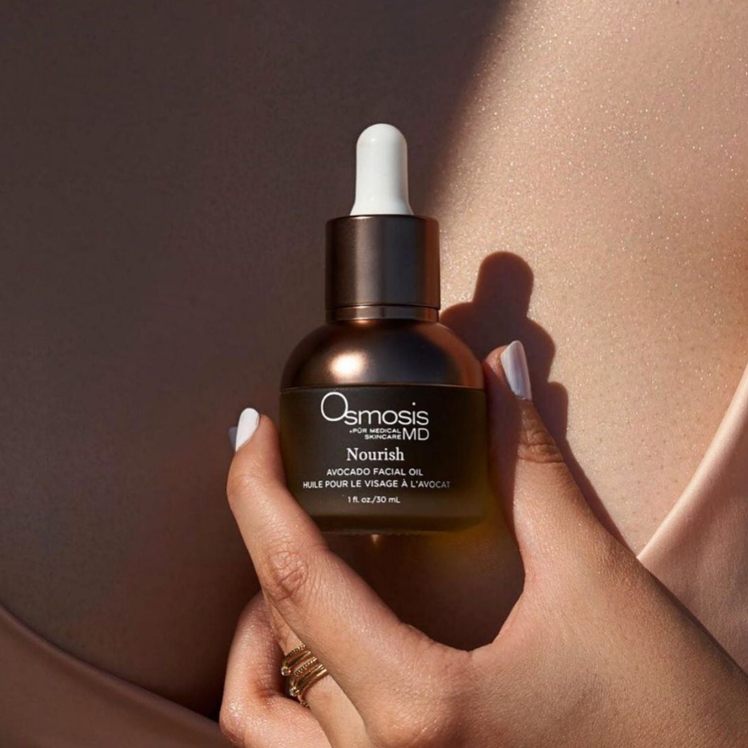 Osmosis Nourish Avocado Facial Oil held by a hand against chest