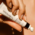 Hand holding a skincare product labeled 'Osmosis' against a neutral background