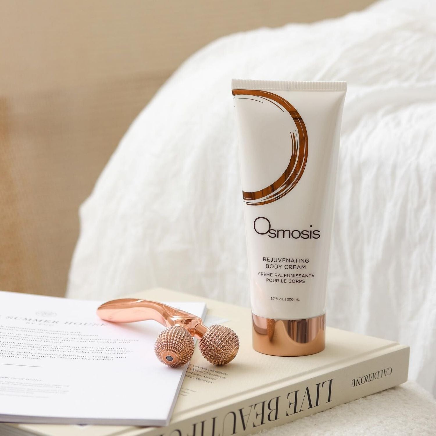 Osmosis Rejuvenating Body Cream on a book with a roller tool