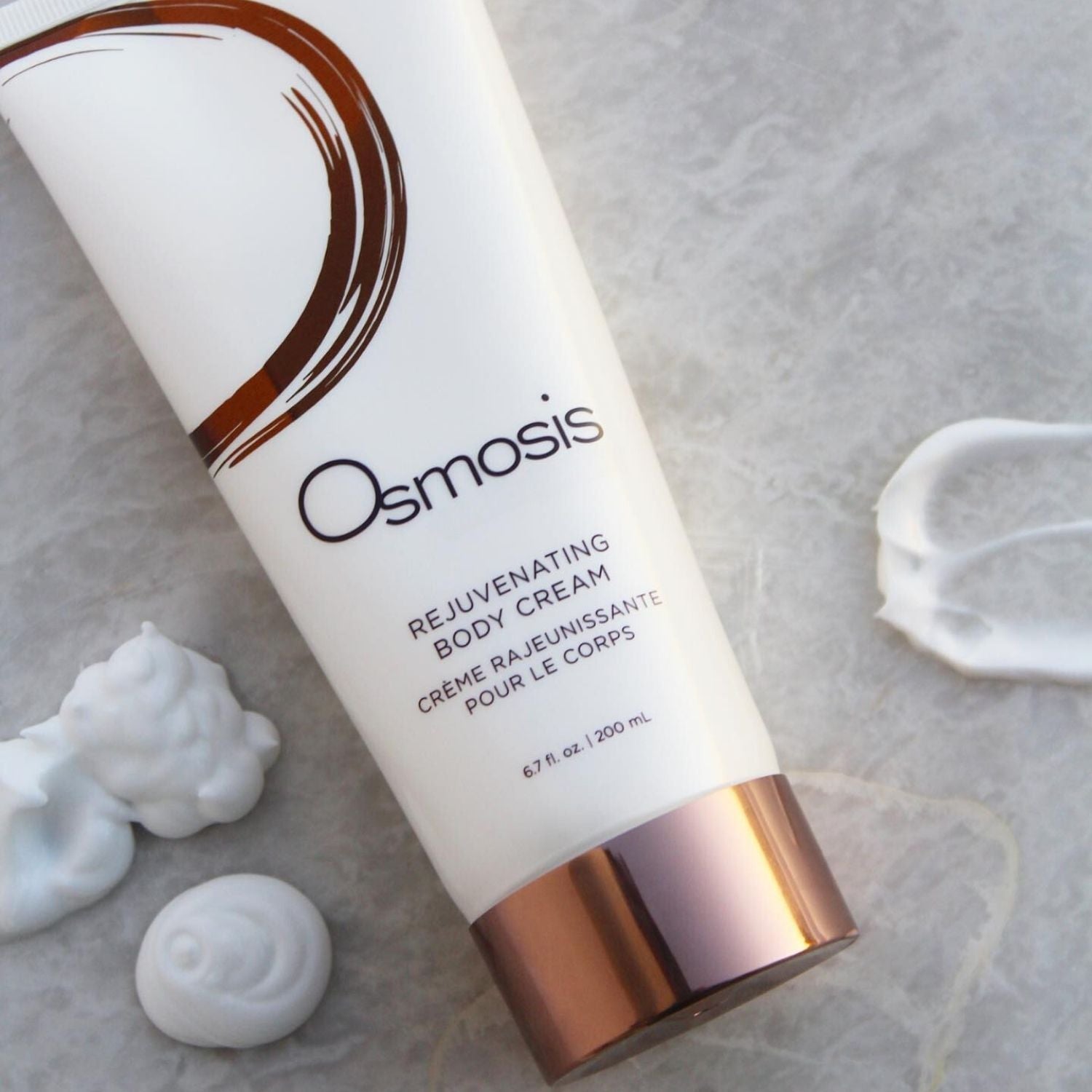 Osmosis Rejuvenating Body Cream on a textured surface with visible cream.
