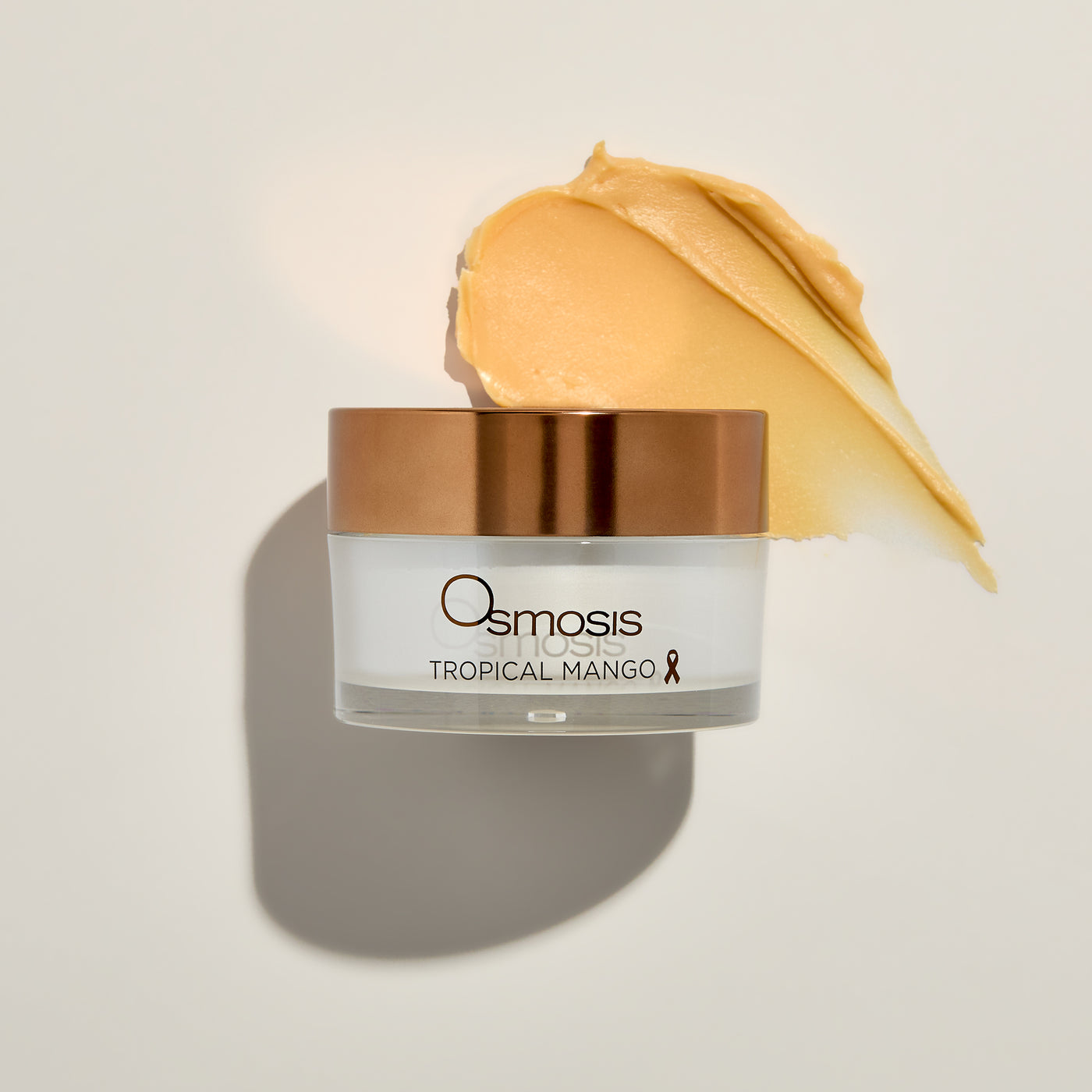 Osmosis Tropical Mango cream jar with a swatch of cream on a beige background